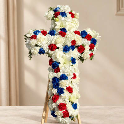Cross-shaped floral tribute with white, red, and blue flowers on an easel