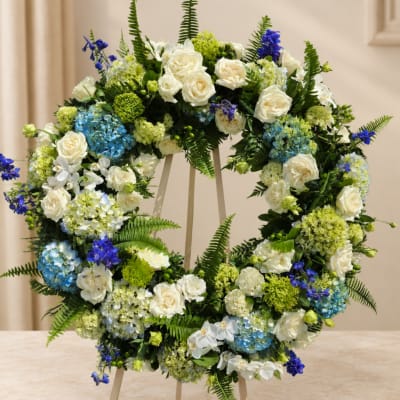 Circular floral wreath with white roses, blue hydrangeas, and purple accents