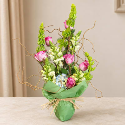 Pink roses and snapdragons in a green wrapped vase arrangement