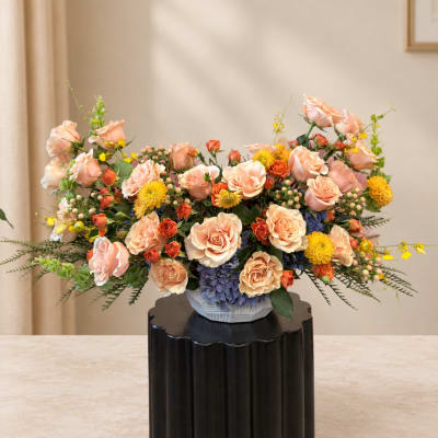 Peach and yellow floral arrangement in a white vase on a black pedestal