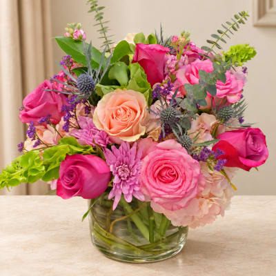 Pink and peach roses in a clear glass vase with purple accents