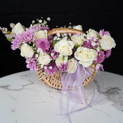 Basket arrangement of white roses and purple daisies with a lavender ribbon
