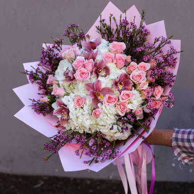 Pink roses and white hydrangeas in a wrapped bouquet with purple accents