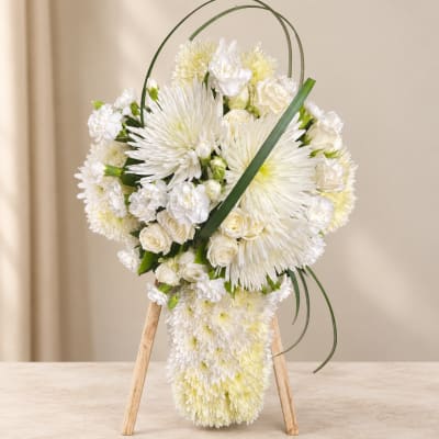 White floral arrangement on a wooden stand with arching greenery