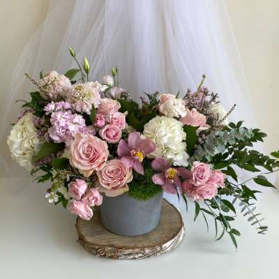 Pink and white floral arrangement in a gray vase with trailing greenery