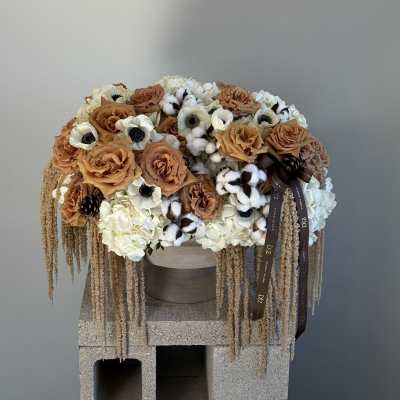Large arrangement of tan roses, white blooms, and cotton stems in a round container