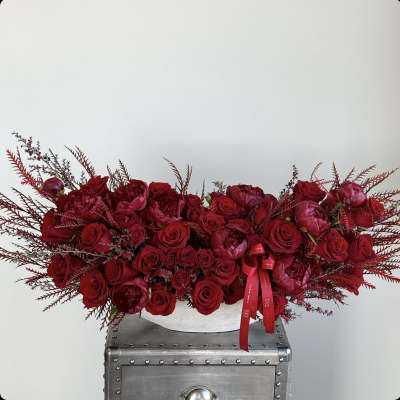 Long red rose arrangement in a white container with a red ribbon