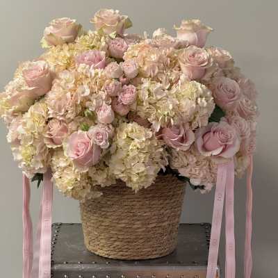 Pink roses and hydrangeas in a woven basket with ribbon tails