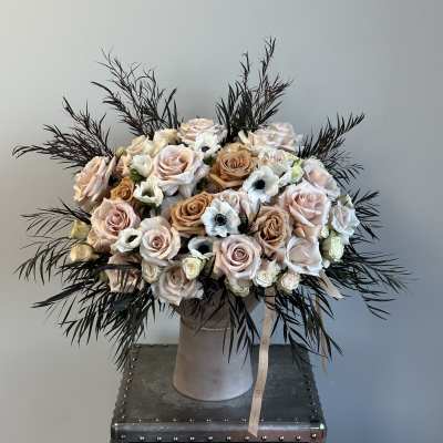 Blush and ivory rose bouquet in a tall vase with dark feathery foliage