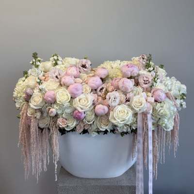 Large pastel floral arrangement in a white container with trailing ribbons