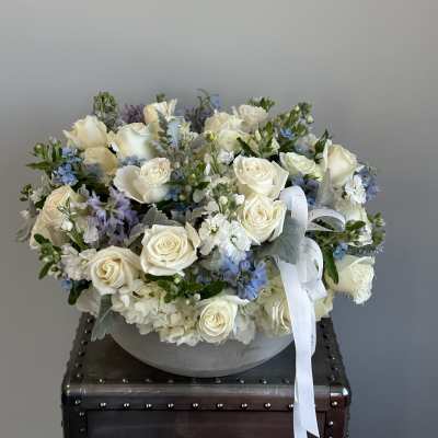 White rose and blue flower arrangement in a round gray vase