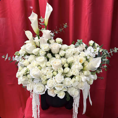 Large white floral arrangement with calla lilies and roses in a black container