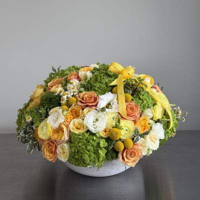 Round floral arrangement with peach and white roses in a low gray bowl