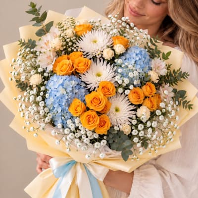 Bouquet of orange roses, blue hydrangeas, and white daisies wrapped in pale paper