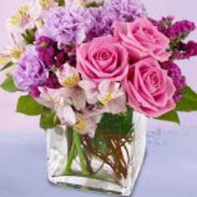 Pink roses and purple flowers arranged in a clear square vase