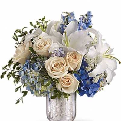 Bouquet of white lilies, cream roses, and blue flowers in a glass vase