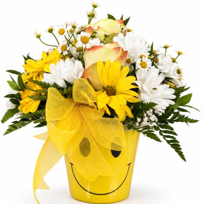 Yellow and white flower arrangement in a smiley-face pot with a yellow bow