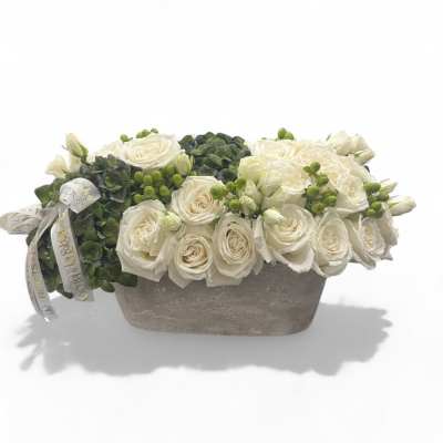 White roses arranged in a low rectangular vase with green berries