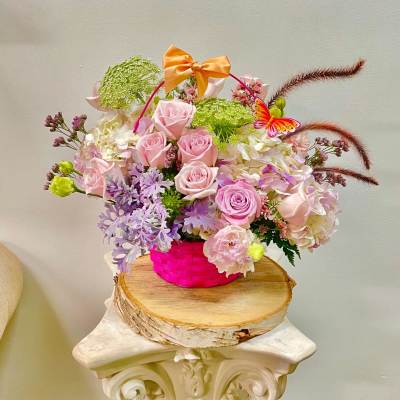 Pink roses and pastel flowers in a bright pink basket with a bow