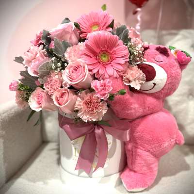Pink flower arrangement with a plush teddy bear in a white hatbox