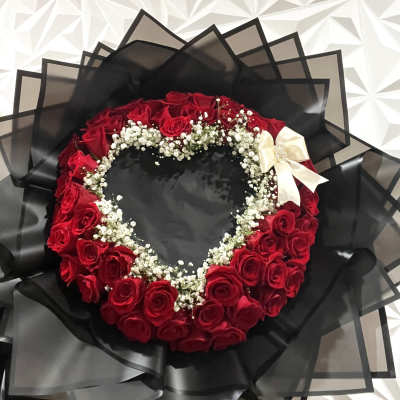 Heart-shaped bouquet of red roses with white baby's breath and a cream ribbon
