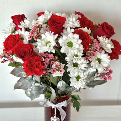 Red roses and white daisies in a red glass vase with a ribbon