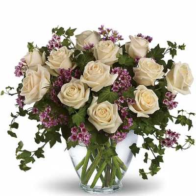 Cream roses and purple filler flowers in a clear glass vase