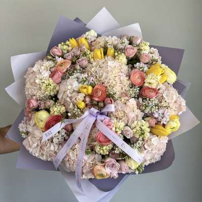 Large pastel bouquet of roses, hydrangeas, and yellow tulips wrapped in lavender paper