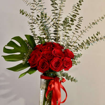 Red roses in a tall glass vase with eucalyptus and a red ribbon
