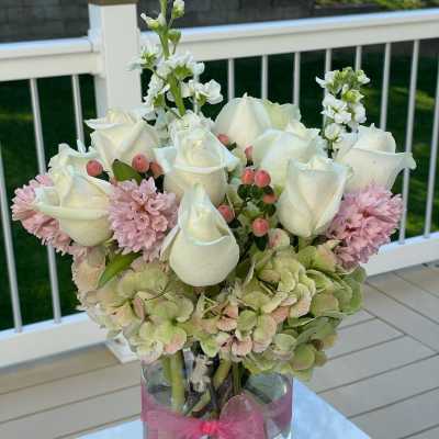 White roses and pink flowers arranged in a glass vase with a pink ribbon