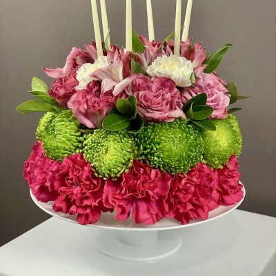 Pink and green floral centerpiece with white candles on a pedestal stand