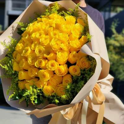 Large bouquet of yellow roses wrapped in beige paper with ribbon