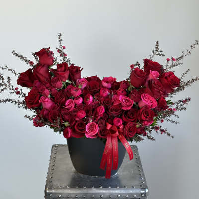 Red and pink rose arrangement in a black vase with ribbon