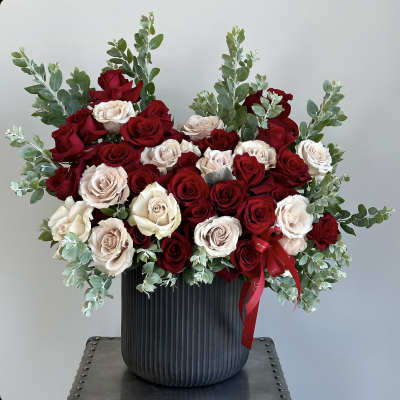 Red and blush roses arranged in a black vase with eucalyptus