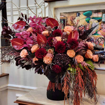 Large floral arrangement with burgundy, pink, and peach blooms in a black vase