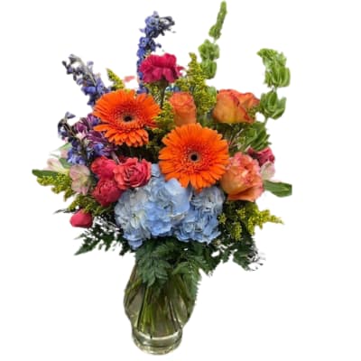 Mixed bouquet with orange gerbera daisies, blue hydrangeas, and roses in a glass vase