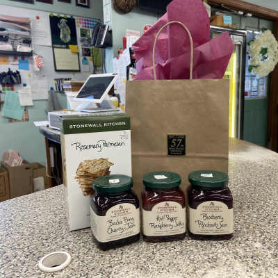 Gift bag with tissue paper, crackers, and three jars of jam on a counter