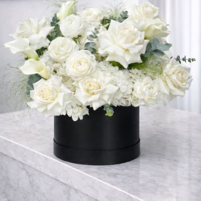 White roses and calla lilies arranged in a black round box