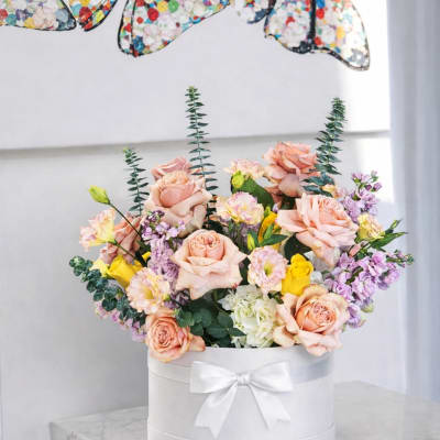 Peach and lavender roses arranged in a white round box with a ribbon bow.