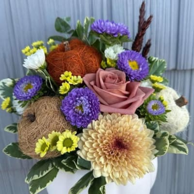 Mixed bouquet with a pink rose, purple daisies, and decorative balls in a white vase