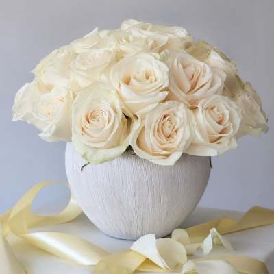 Cream rose bouquet in a white textured vase with pale ribbon