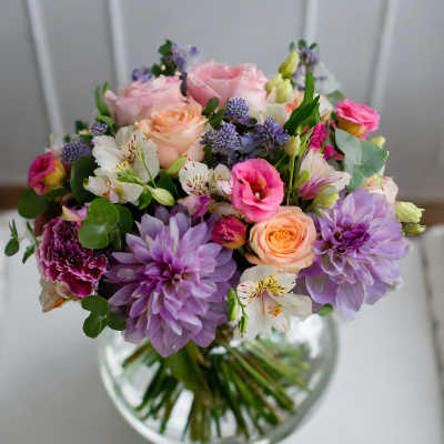 Mixed bouquet of pink, peach, and lavender flowers in a glass vase