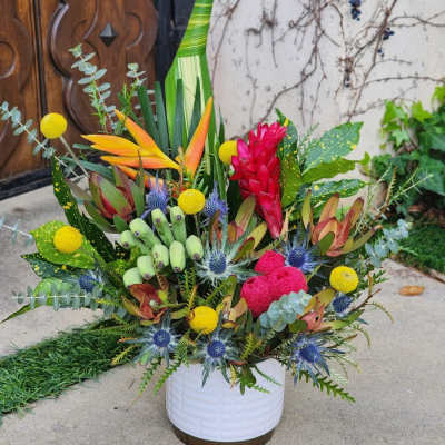 Tropical floral arrangement in a white container with bright red, yellow, and blue accents