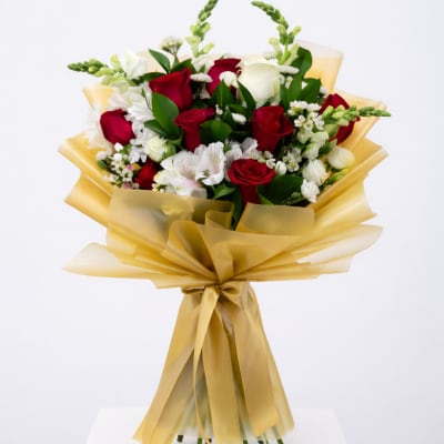 Hand-tied bouquet of red and white roses with white accent flowers wrapped in gold cellophane and ribbon.