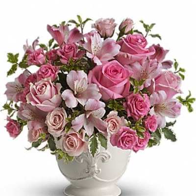 Pink roses and lilies arranged in a white pedestal vase