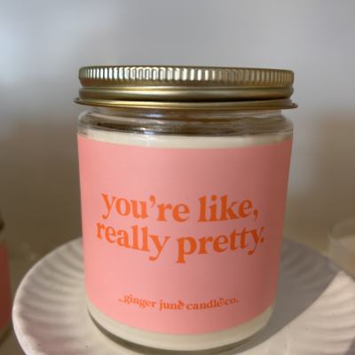 Pink-labeled jar candle with gold lid on a white ceramic pedestal stand