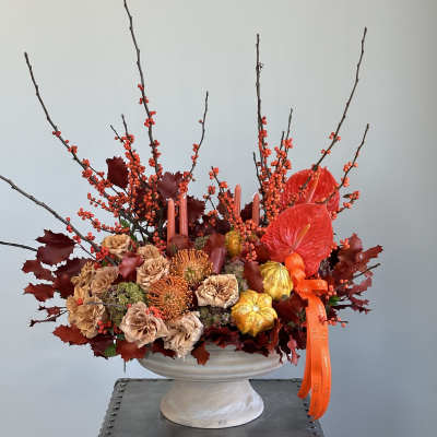 Autumn floral arrangement in a white pedestal vase with orange ribbon