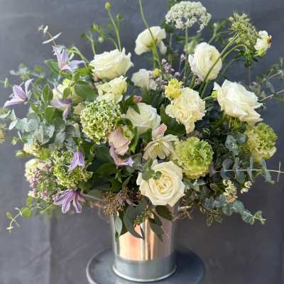 White roses and green blooms in a metal vase with purple flowers
