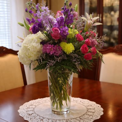 Mixed bouquet of purple, pink, white, and yellow flowers in a clear glass vase