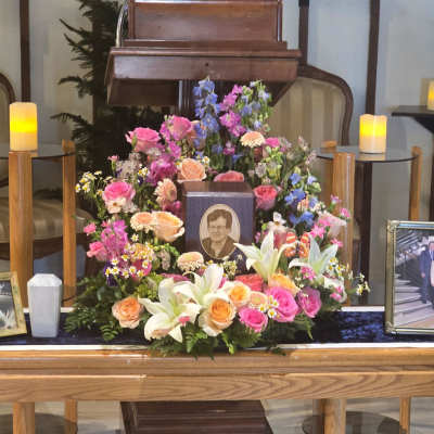 Large funeral flower arrangement with pink, peach, white, and blue blooms